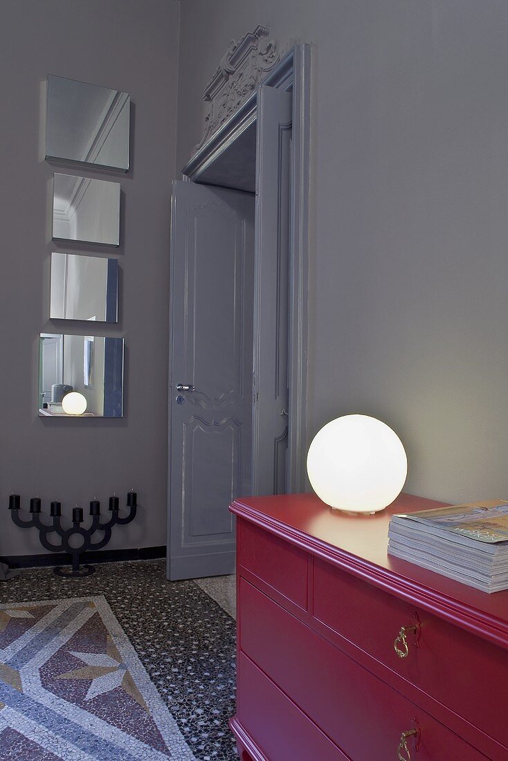 A ball-shaped lamp on a red chest of drawers and an artistic mirror installation