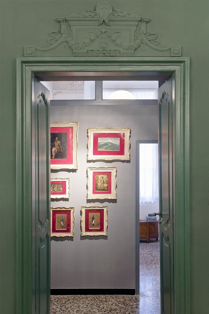 Blick durch zwei-flügelige Tür auf Wand mit Bildersammlung in rotem Passepartout