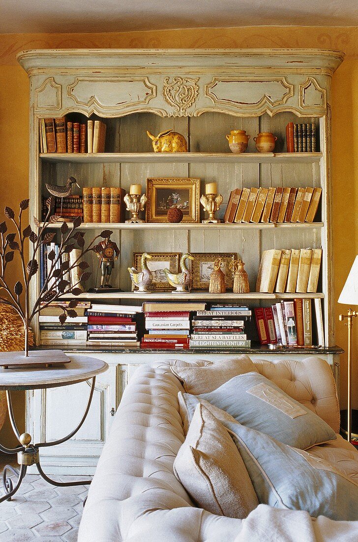 An antique dresser of books against a coloured wall and a light-coloured upholstered sofa