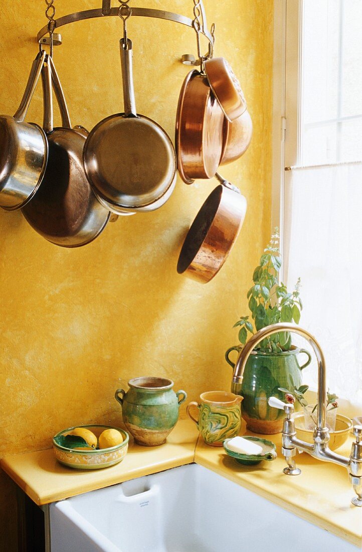 Gelbgetönte Küchenecke - gehängte Kupferpfannen und Spüle vor Fenster