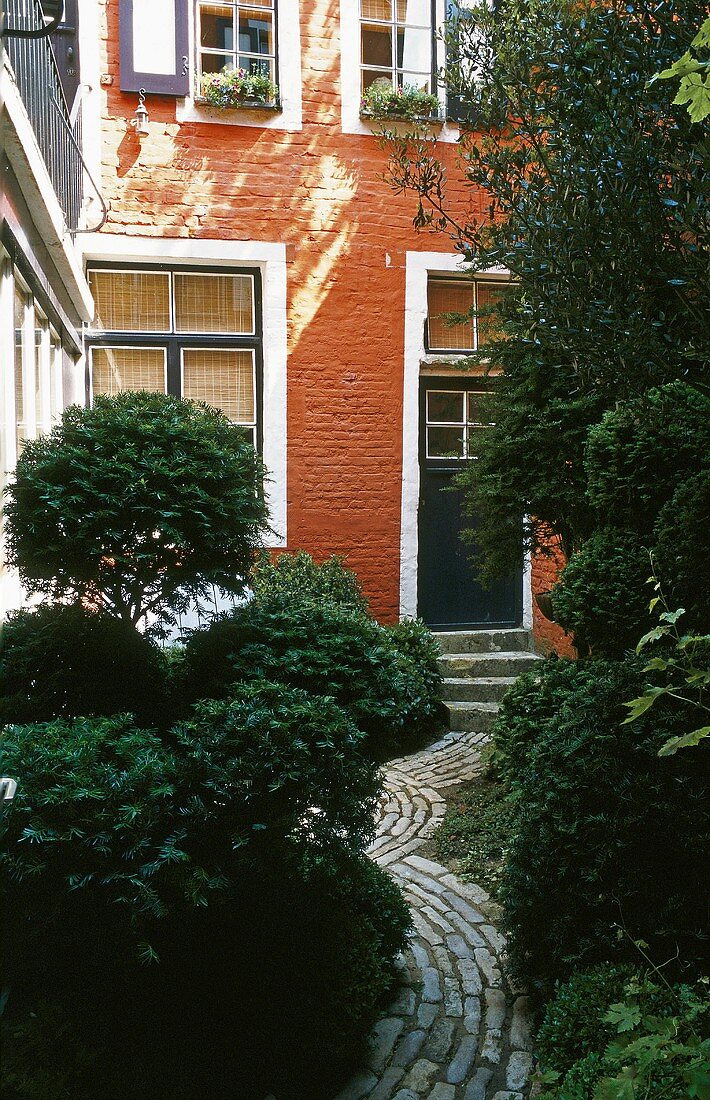 Wohnhaus mit roter Fassade und Weg im grünen Hinterhof