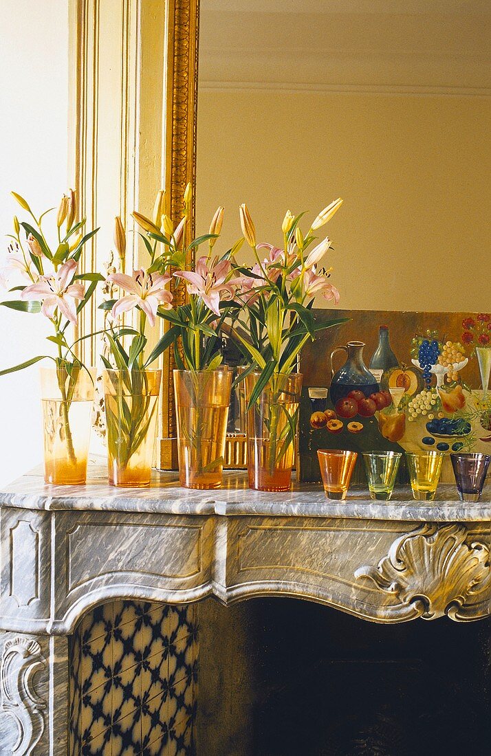 An arrangement of lilies in an orange vase and tea lights on the mantelpiece