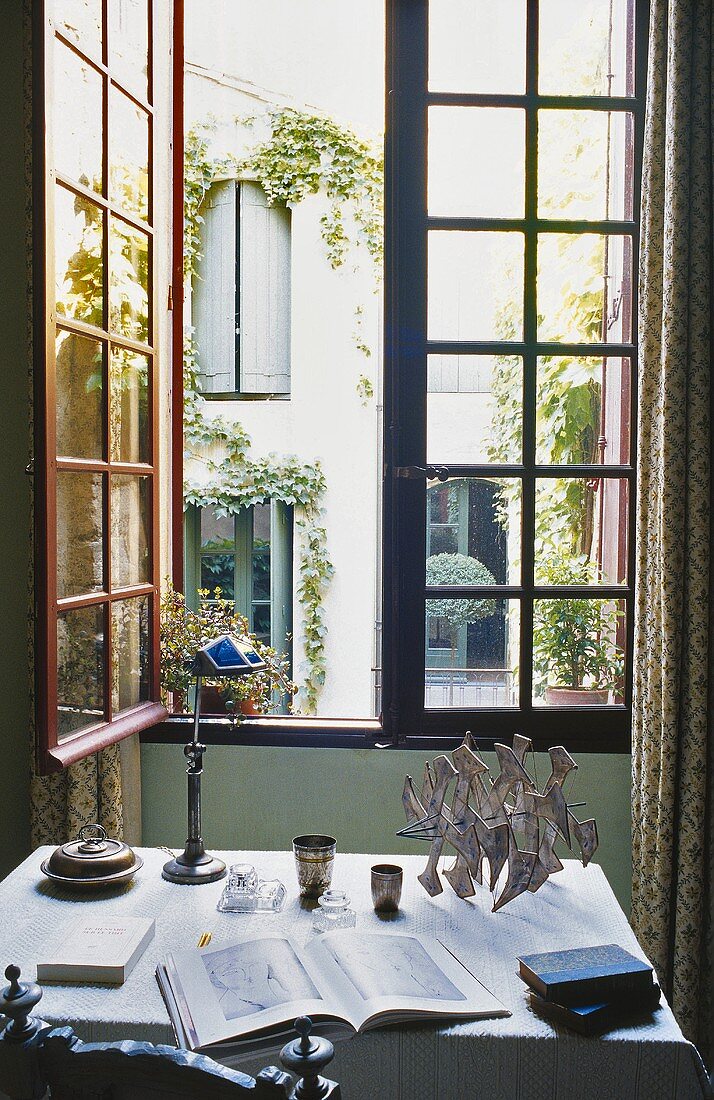 A desk in front of an open window with a view of a courtyard