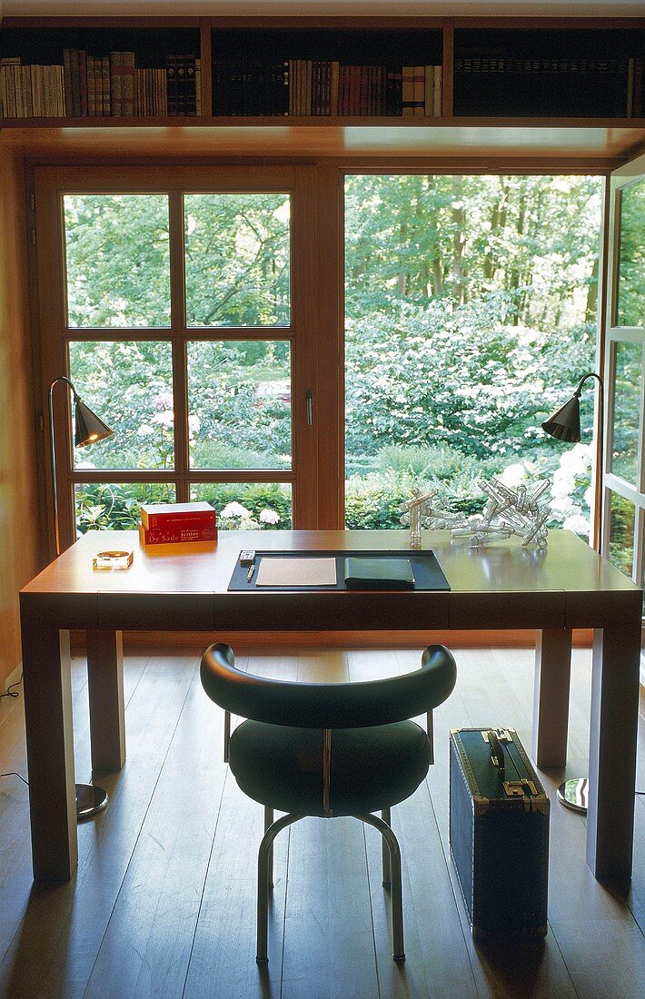 Arbeitstisch mit Lederstuhl aus Bauhauszeit vor geöffneter Terrassentür mit Gartenblick