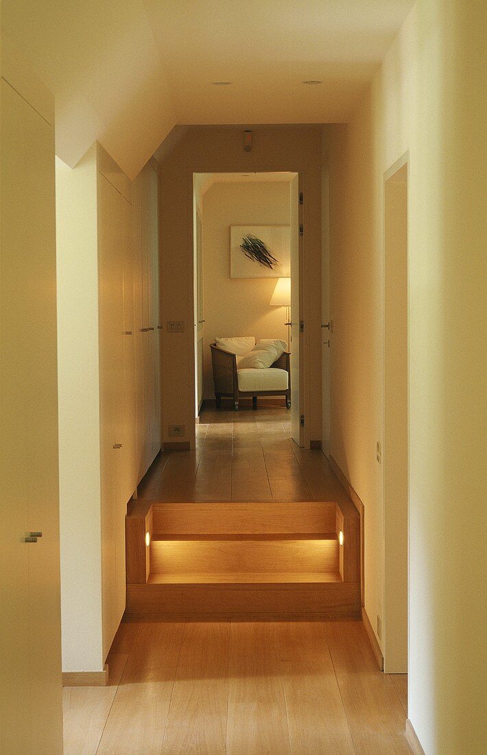A hallway with illuminated steps and a view through an open door onto an armchair