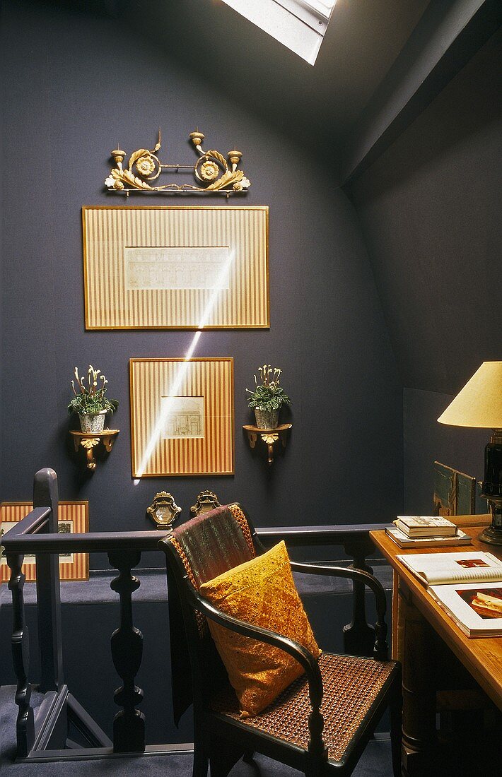 Under the roof - a dark grey wall hung with gold-framed pictures and an office corner on the landing