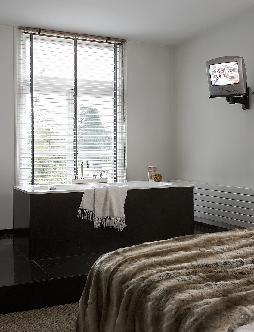 Felldecke auf Bett und freistehende graue Badewanne vor Fenster