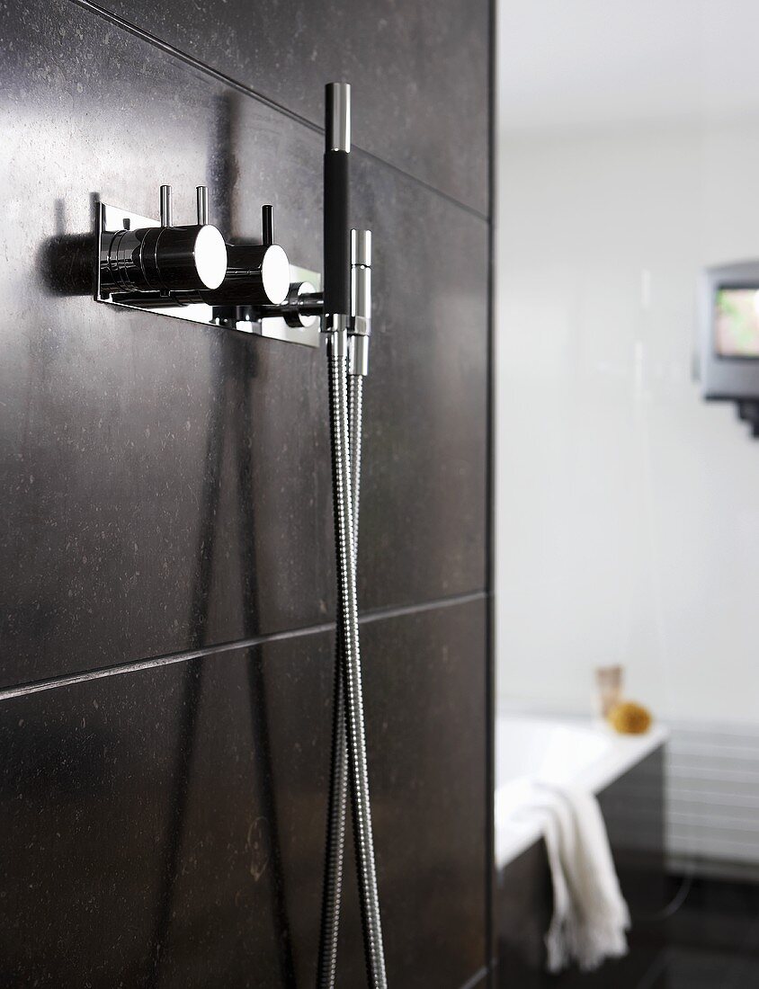Designer taps with a shower head on a grey-tiled shower wall
