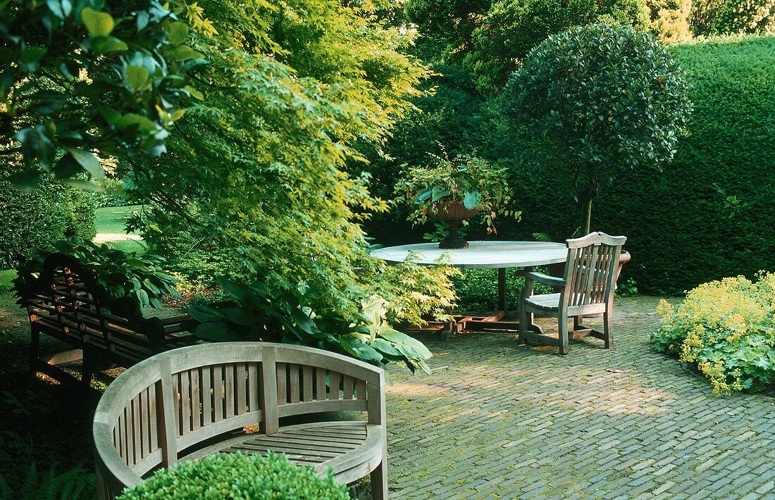 Garten - Holzbank vor Baum und Tisch mit Stuhl auf gepflasterter Terrasse