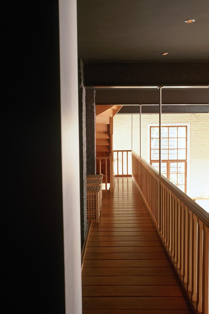 Schmale Holzgalerie mit Geländer unter schwarzer Decke und Blick auf Fenster