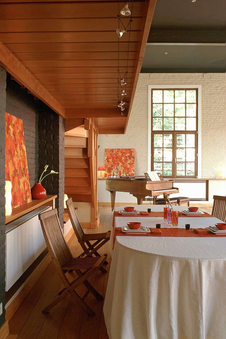 An open living-room-cum-dining-room with a table laid under a gallery with wooden chairs