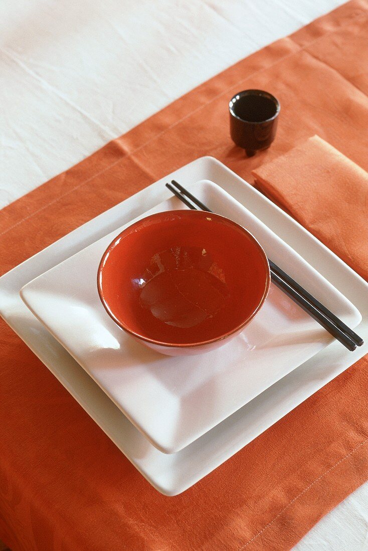 Asiatisches Gedeck - rotes Schälchen auf weissen Tellern mit Essstäbchen