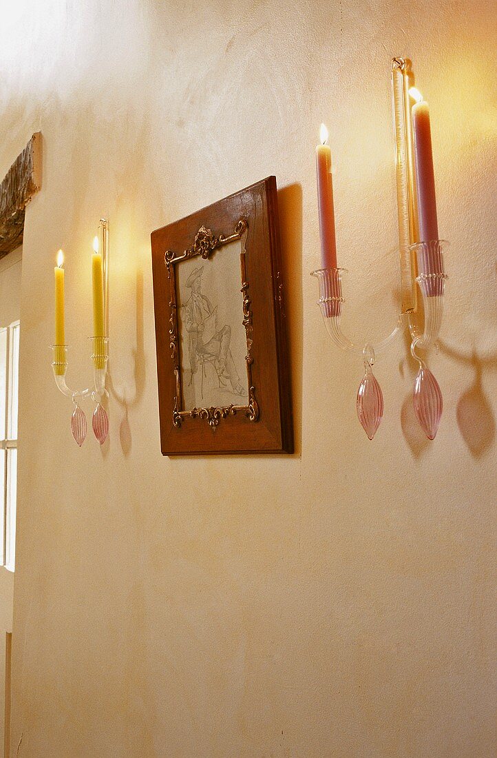 Wandkerzenhalter mit farbigen brennenden Kerzen und gerahmtem Bild