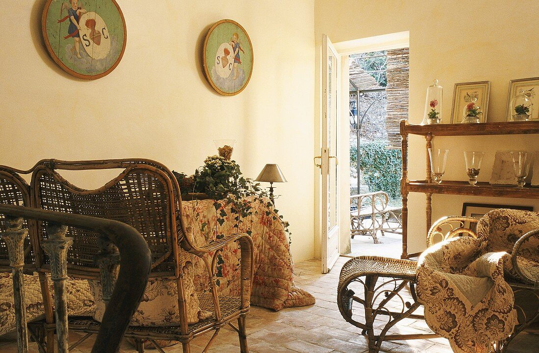Korbmöbel mit Polster und Wandregal mit Vasen im ländlichen Wohnraum und Blick auf offene Gartentür
