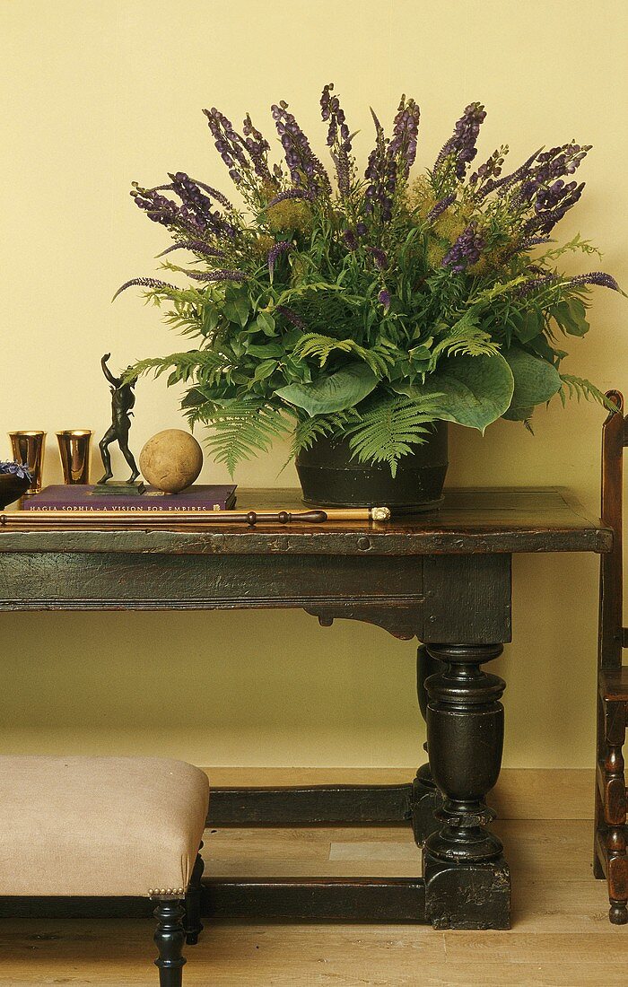 A flower arrangement with purple flowers on a rustic side table in front of a yellow wall