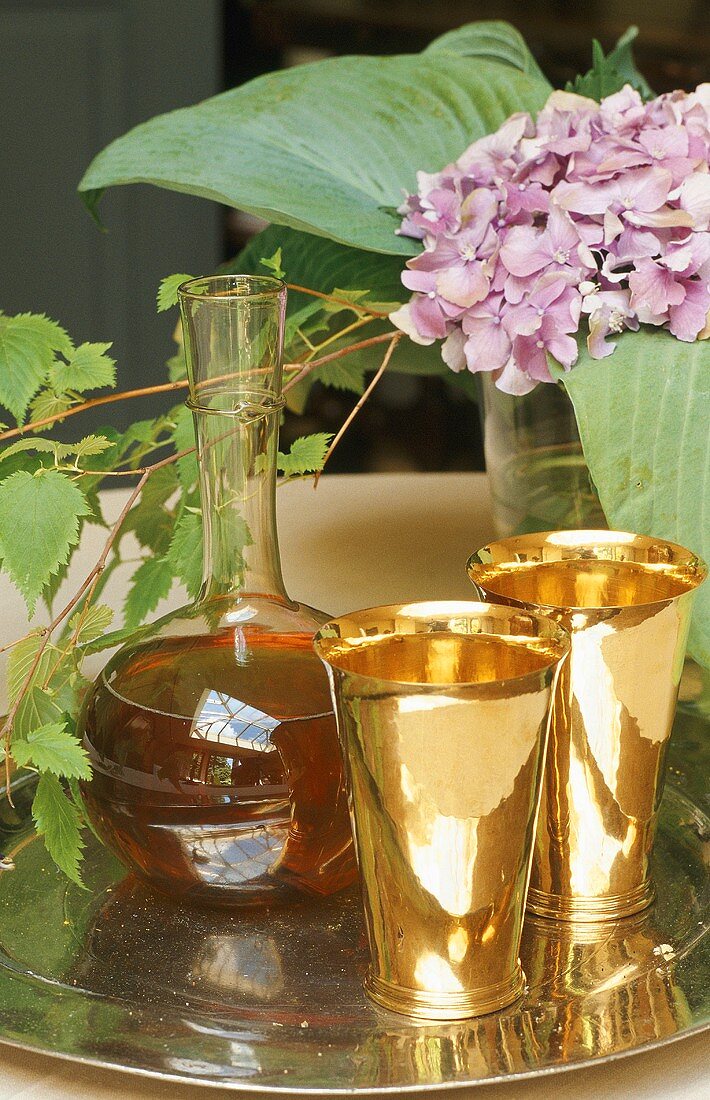 Still life on a silver tray - brass cups with a carafe of wine and flowers