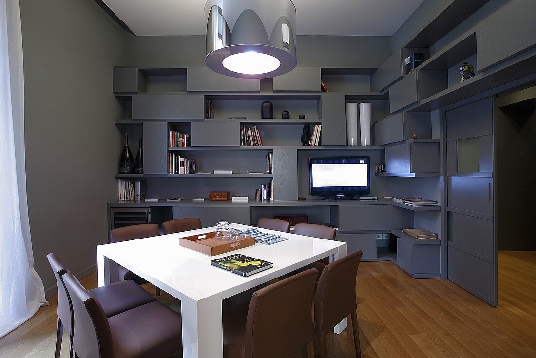 A designer living room in grey - a white table and metal lampshades in front of a wall with built-in shelving