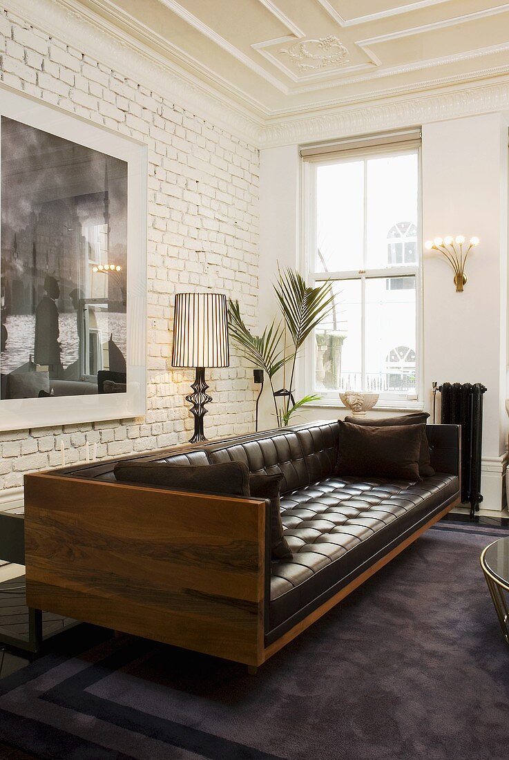 An elegant leather sofa with a wooden frame in front of a white brick wall