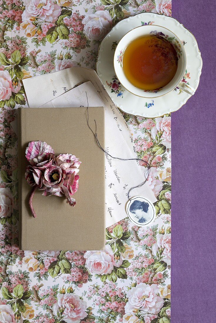 Tasse Tee neben Buch auf Papier mit Blumenmuster