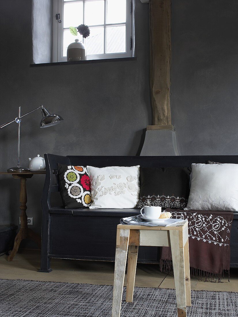 Side table in from of a black bench with white pillows in front of a gray wall