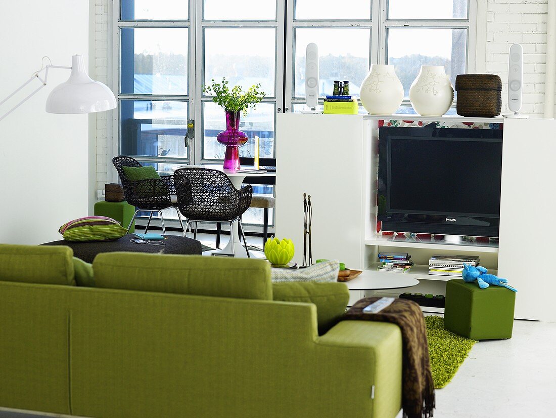 Grünes Sofa und halbhoher weisser Medienschrank mit Blumenvasen vor Terrassentüren