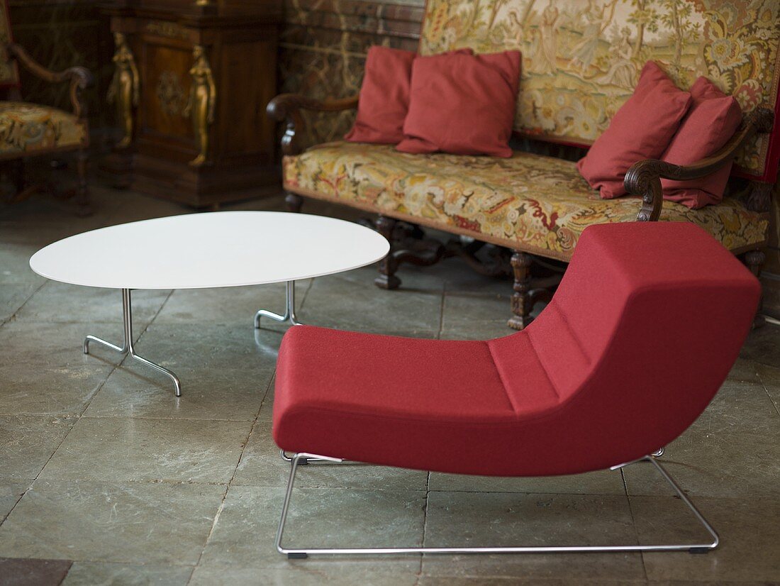 Red upholstered chair with metal frame and white coffee table in front of an antique sofa