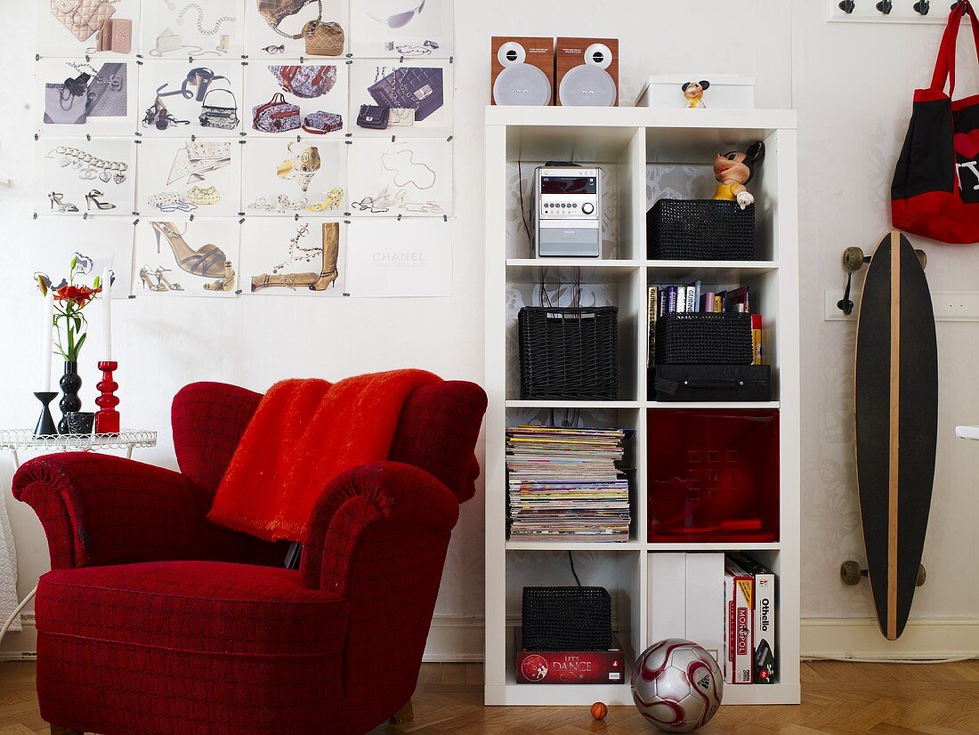 Red upholstered chair and white shelves and a skateboard on the wall