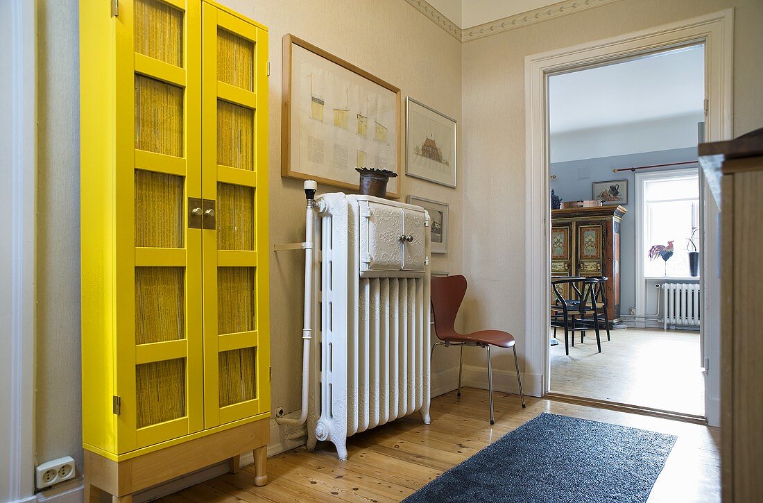 Vorraum mit kräftig gelbem Vitrinenschrank neben Heizkörper und offene Tür mit Blick in Wohnraum