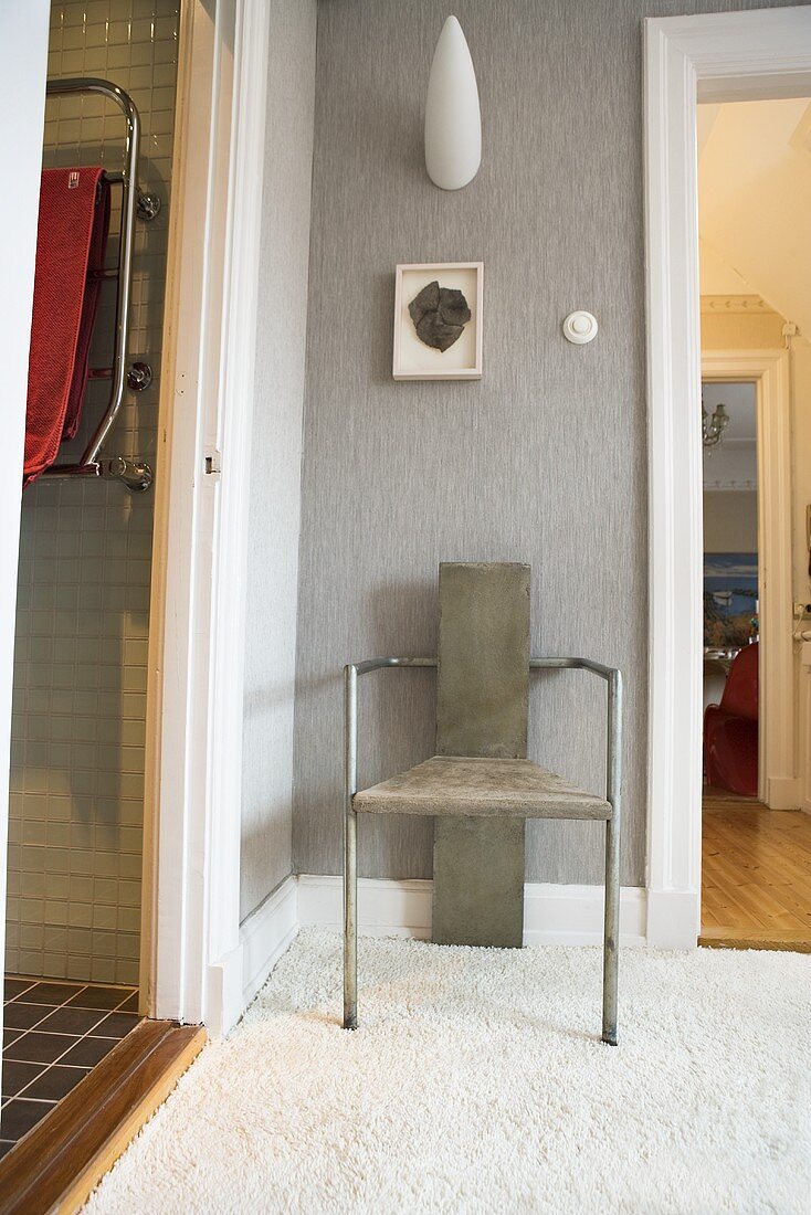 Designerstuhl aus Metall vor grauer Wand mit Designer Wandlampe