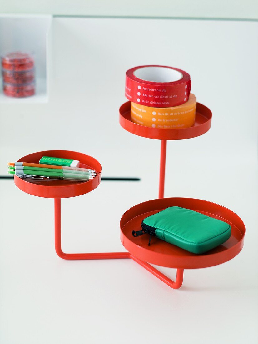 A red metal stand with round trays as a shelf for desk items