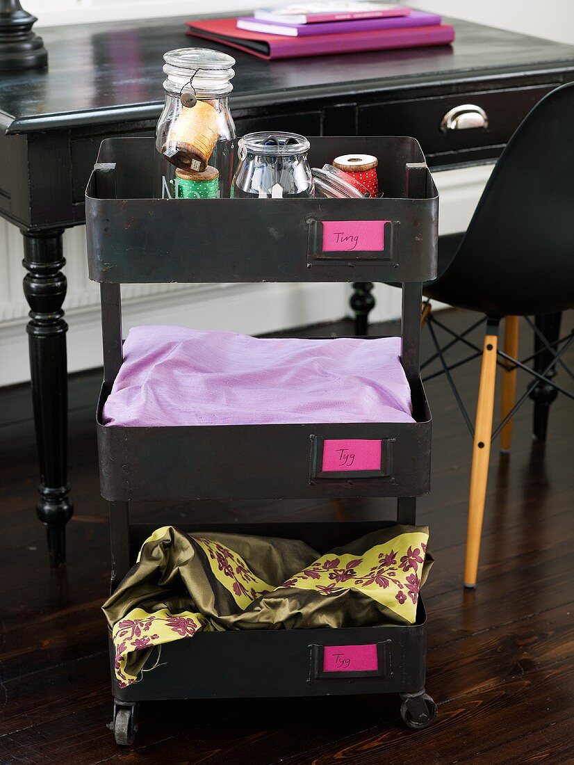 Black rolling storage container with open drawers in front of a black table