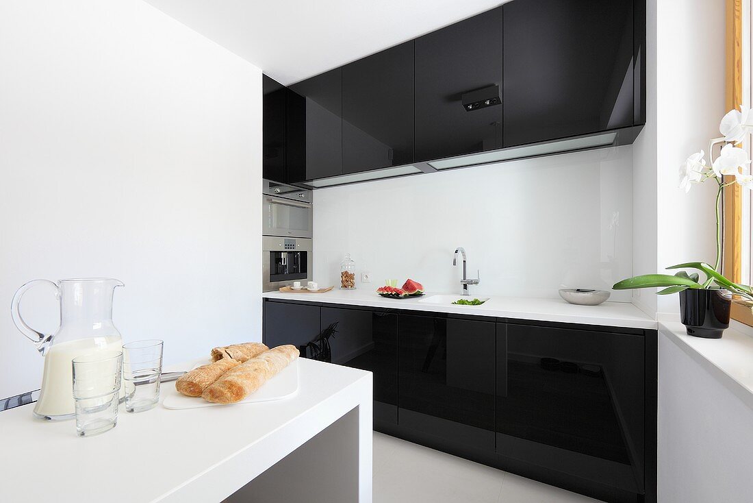 Blick in Küche mit schwarzen Hochglanzfronten & weißem schmalem Esstisch