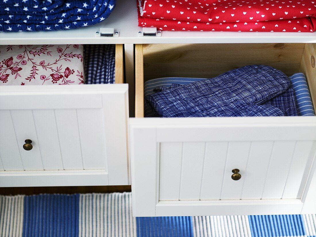 Pads and patterned fabric in drawers with white wooden fronts