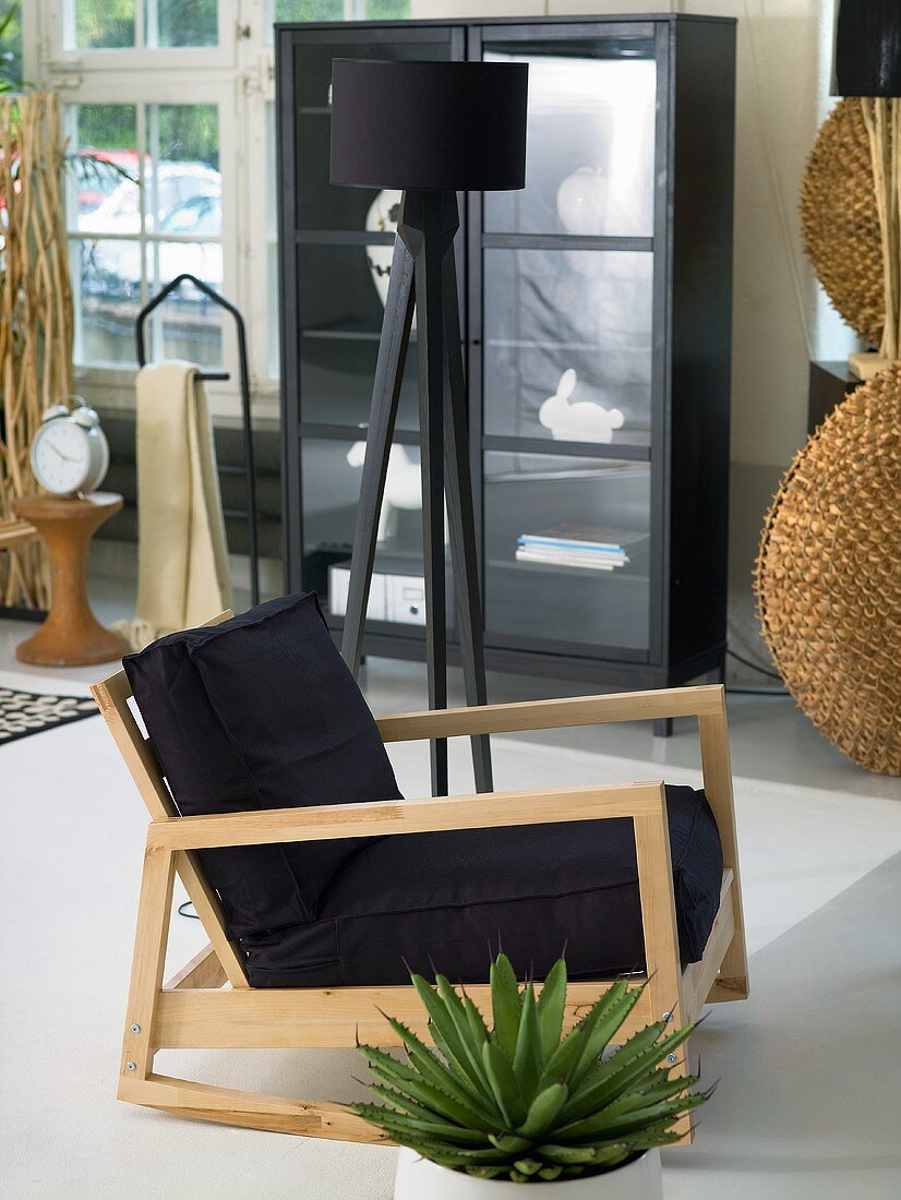 Black upholstery on a chair with a light wood frame and swing frame in front of a black floor lamp