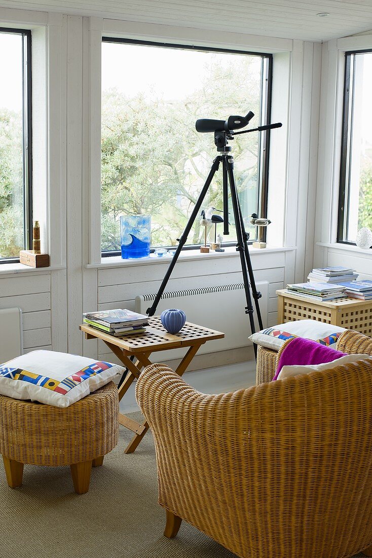 Sessel und Hocker aus Rattan um Beistelltisch aus Holz neben Stativ mit Kamera vor Fensterfront