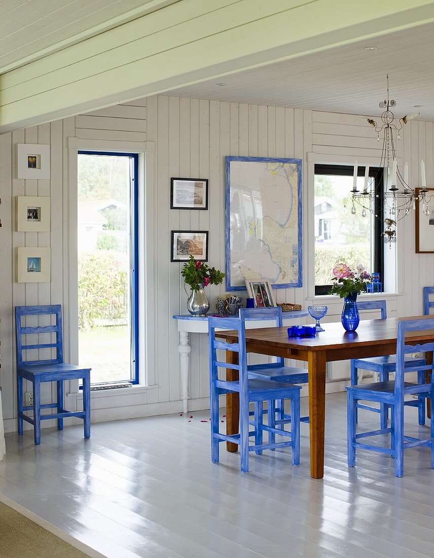 Offener Essraum mit weisser Holzverkleidung und blauen Stühlen am Esstisch vor Gartentür