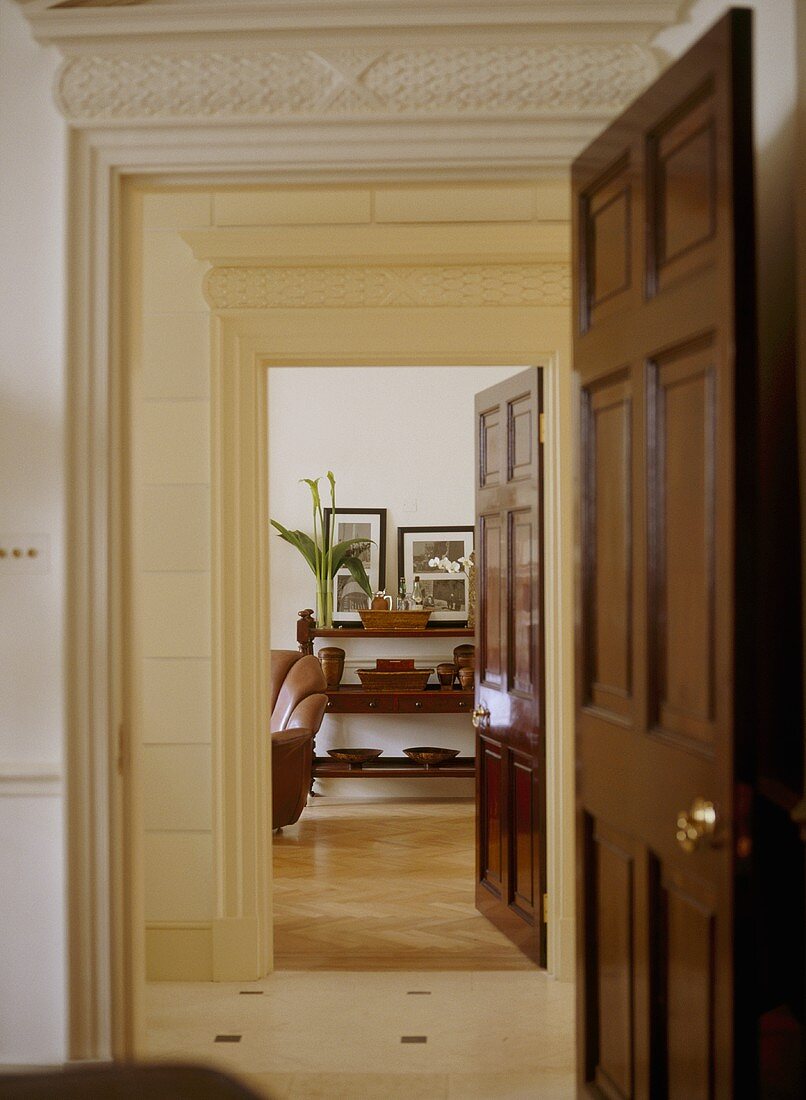 A traditional hallway with a pair of doorways, panelled doors open, ornate plaster work cornices, view into sitting room