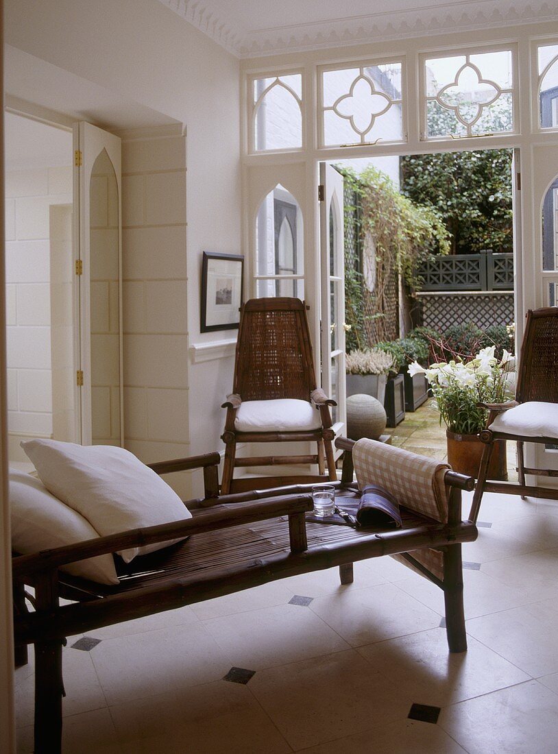 Wohnzimmer im eleganten Landhaus mit Möbeln aus Rattan und offener Gartentür