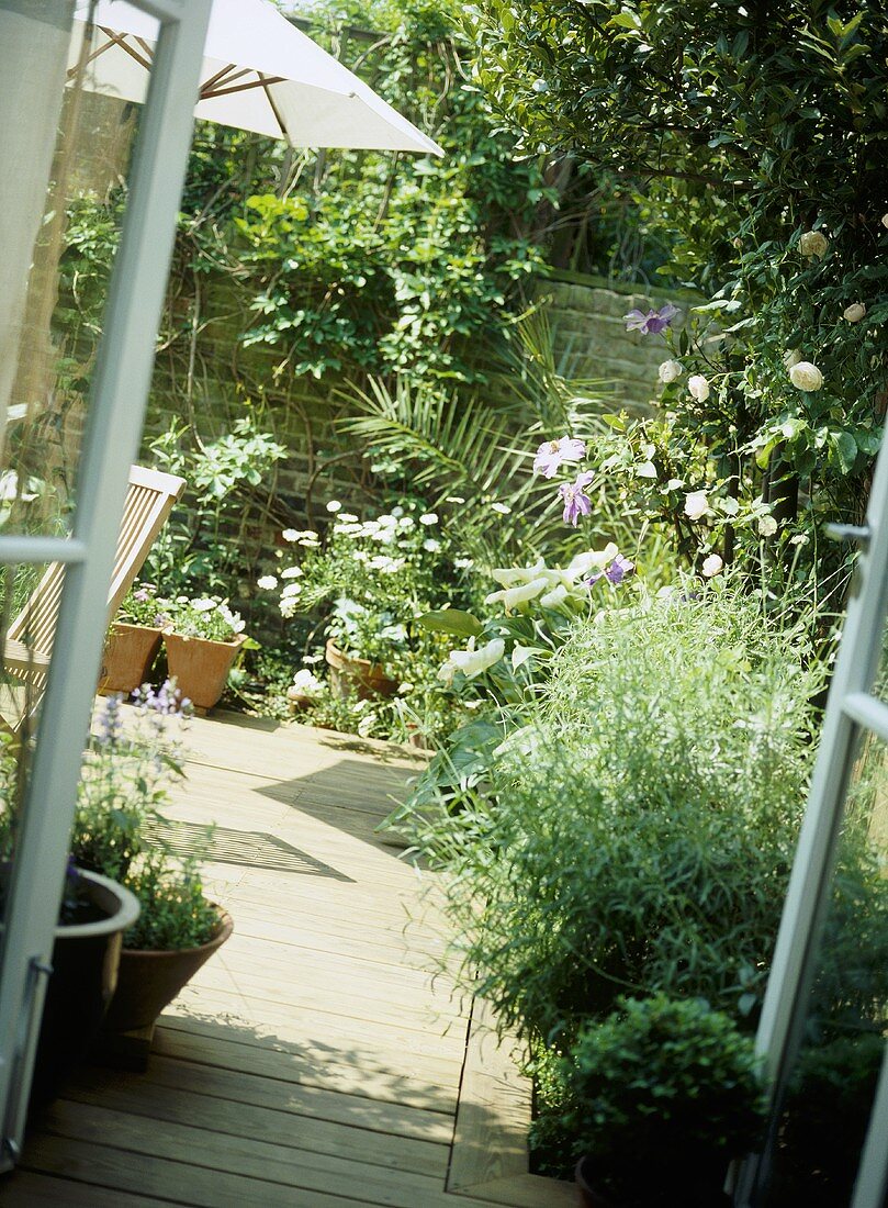 Blick durch Gartentür auf Holzterrasse und Blumenbeeten