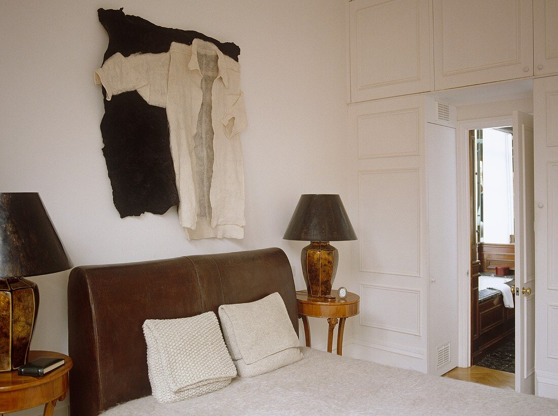 Antike Lampe auf Nachttisch neben Doppelbett mit Kopfteil aus Lederpolster und offene Tür