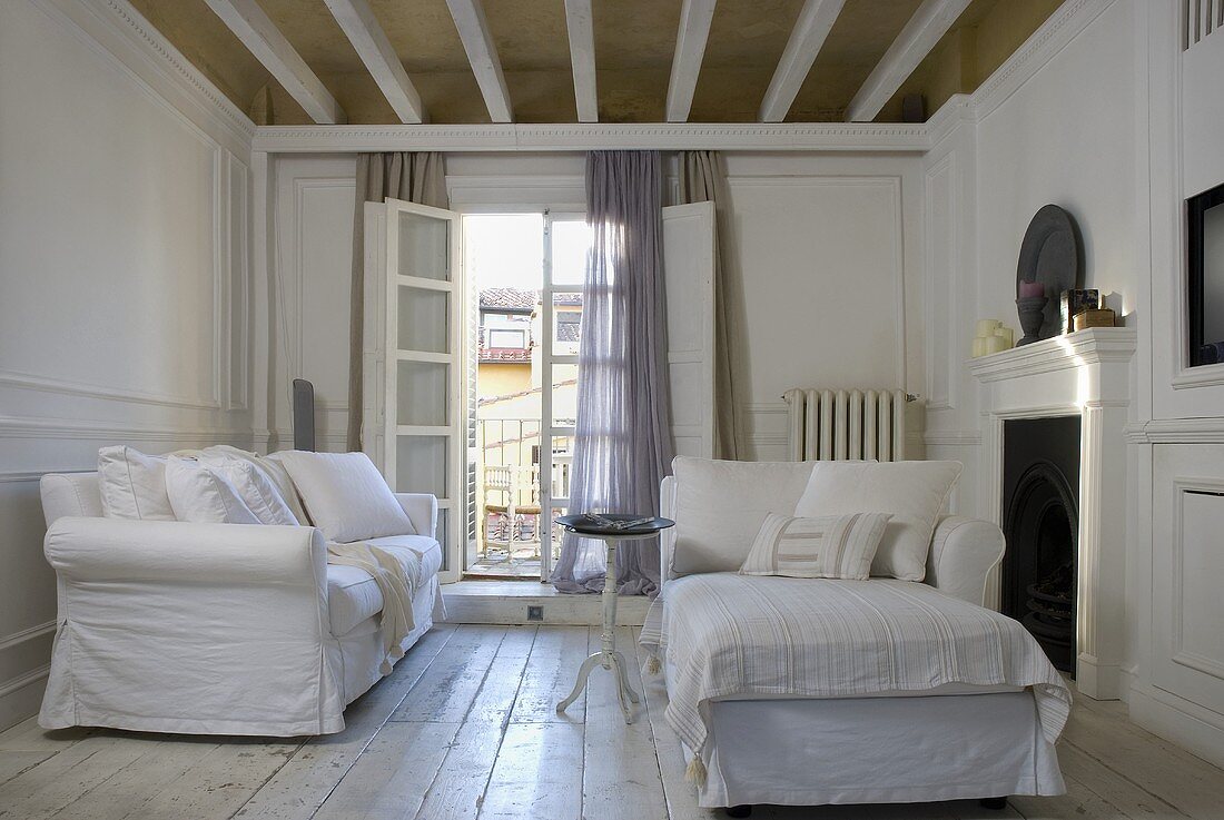 weiße Sofagarnitur mit Hussen vor offener Balkontür und rustikaler Dielenboden