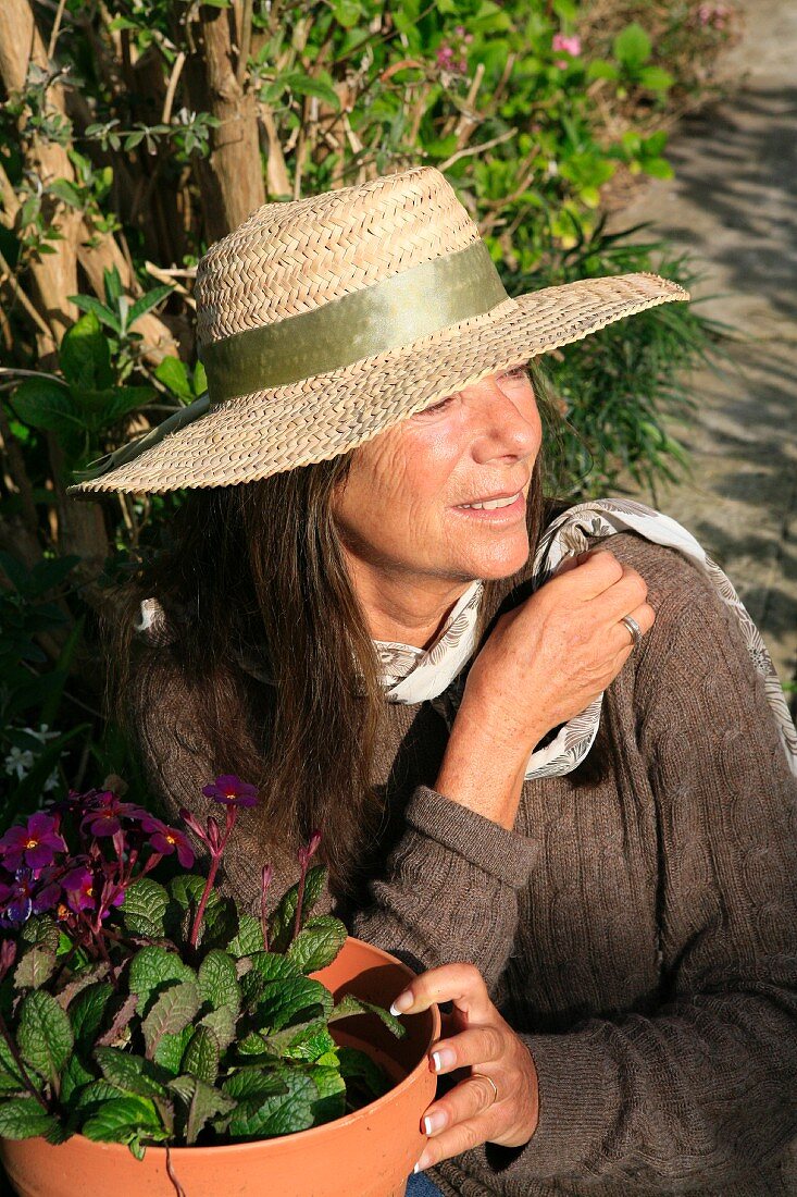 Frau mit Strohhut vor Pflanzentopf im Garten