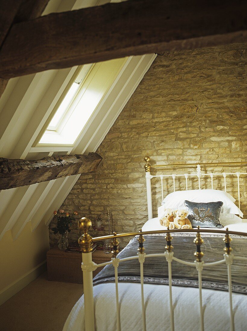 Messing-Bett vor Natursteinwand und unter Dachschräge mit Dachfenster