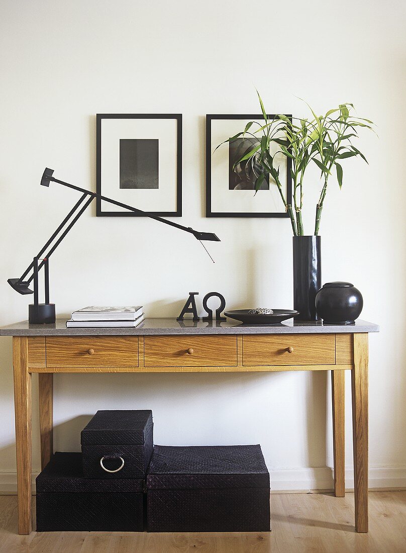 Wandtisch aus Holz mit Schreibtischleuchte und Blumenvase, darunter dreiteiliges Schachtelset