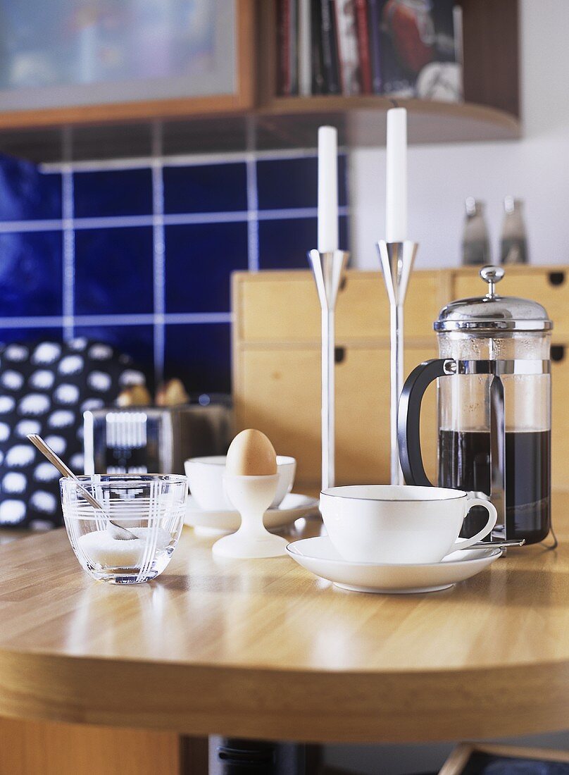 A detail of a modern kitchen, wood breakfast table, cup and saucer, coffee, caffetiere, boiled egg, candlesticks, candles,