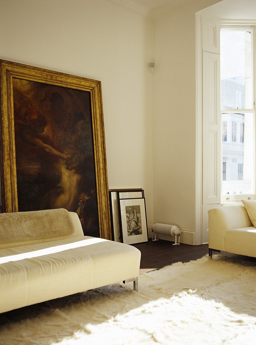 Weisses Polstersofa vor Bild mit Goldrahmen an Wohnzimmerwand lehnend
