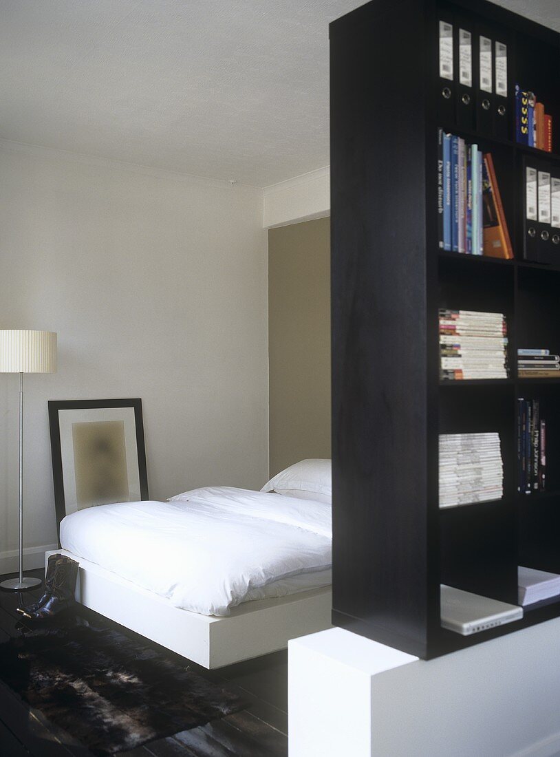 Schwarzes Bücherregal als Raumteiler vor Bett mit weisser Bettwäsche