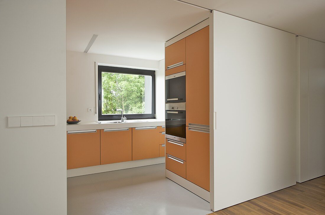 Moderne Küche mit orangefarbenen Fronten und offener weisser Schiebetür