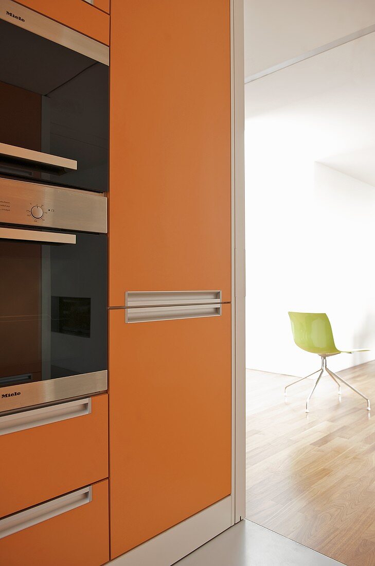 Orangefarbene Fronten am Einbauschrank mit Einbaugeräten in moderner offener Küche