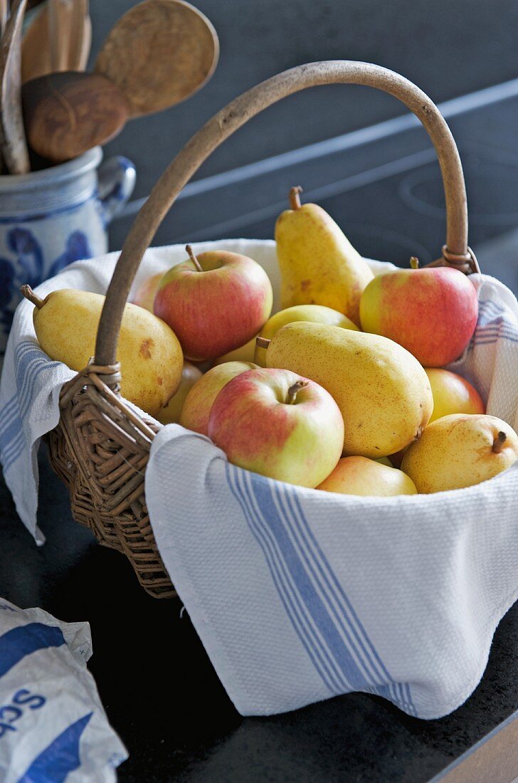 Äpfel und Birnen im Korb mit Geschirrtuch ausgelegt